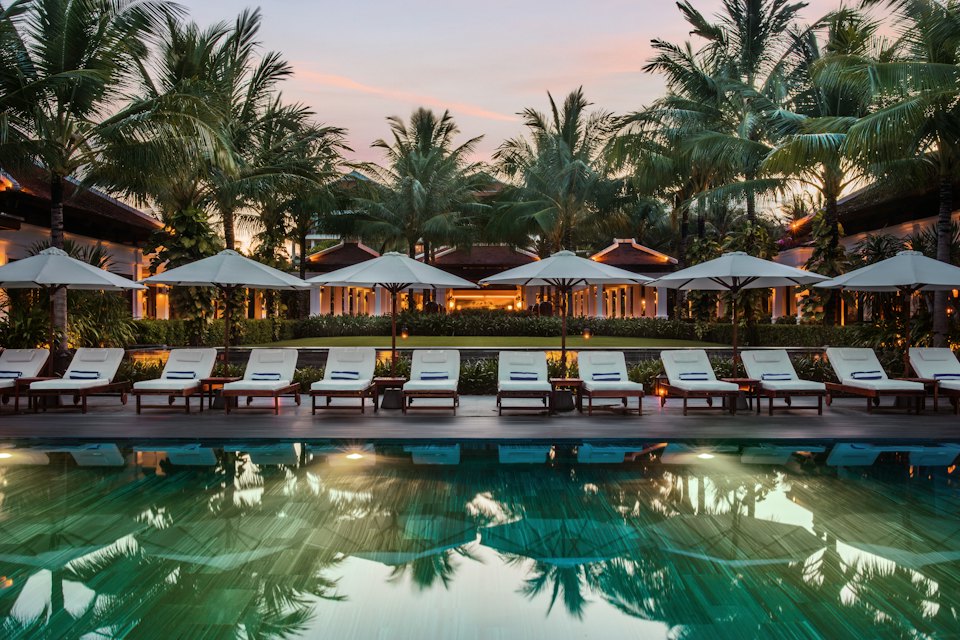 Resort swimming pool lined with palm trees and sun loungers